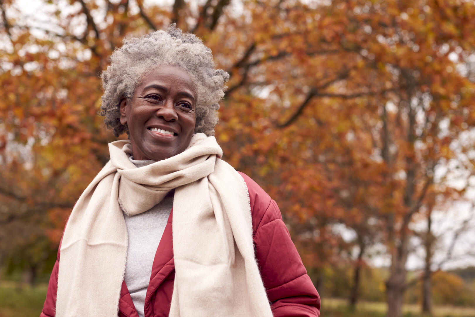 Head And Shoulders Portrait Of Senior Woman On Walk Through Autumn Countryside Against Golden Leaves